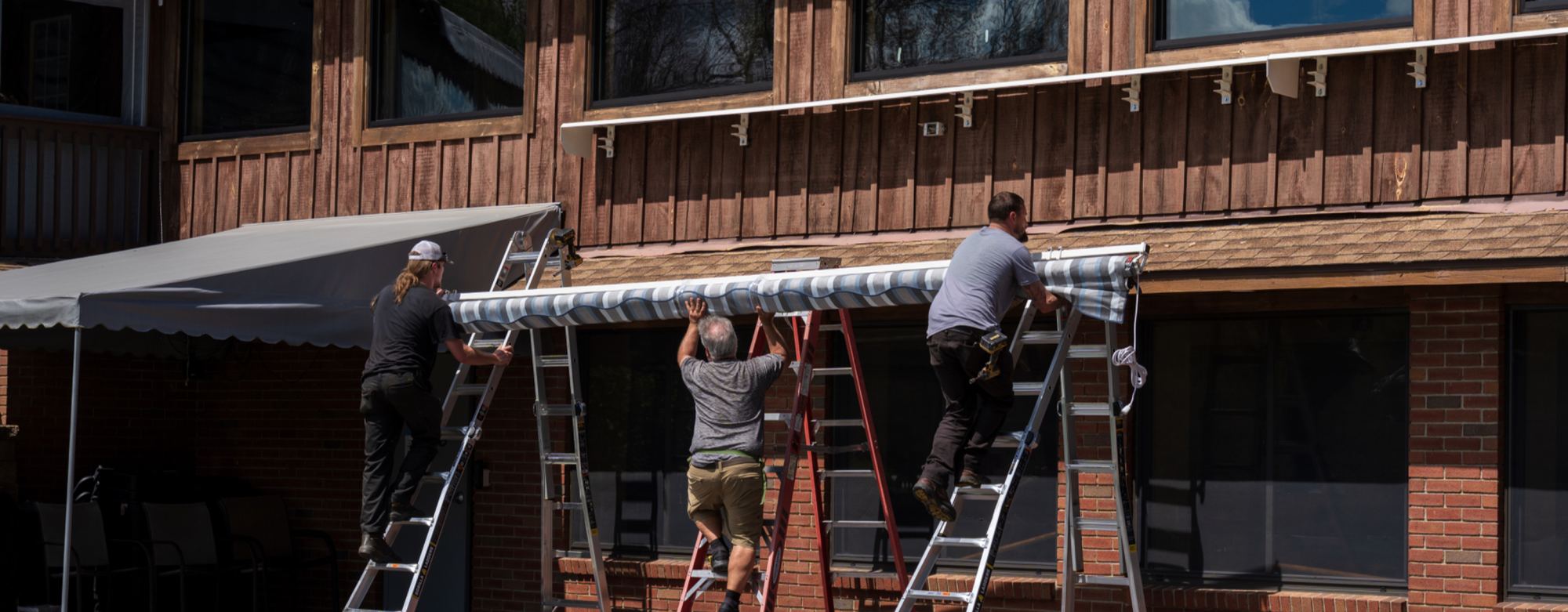 An installation crew on ladders fitting a retractable awning to a commercial building facade