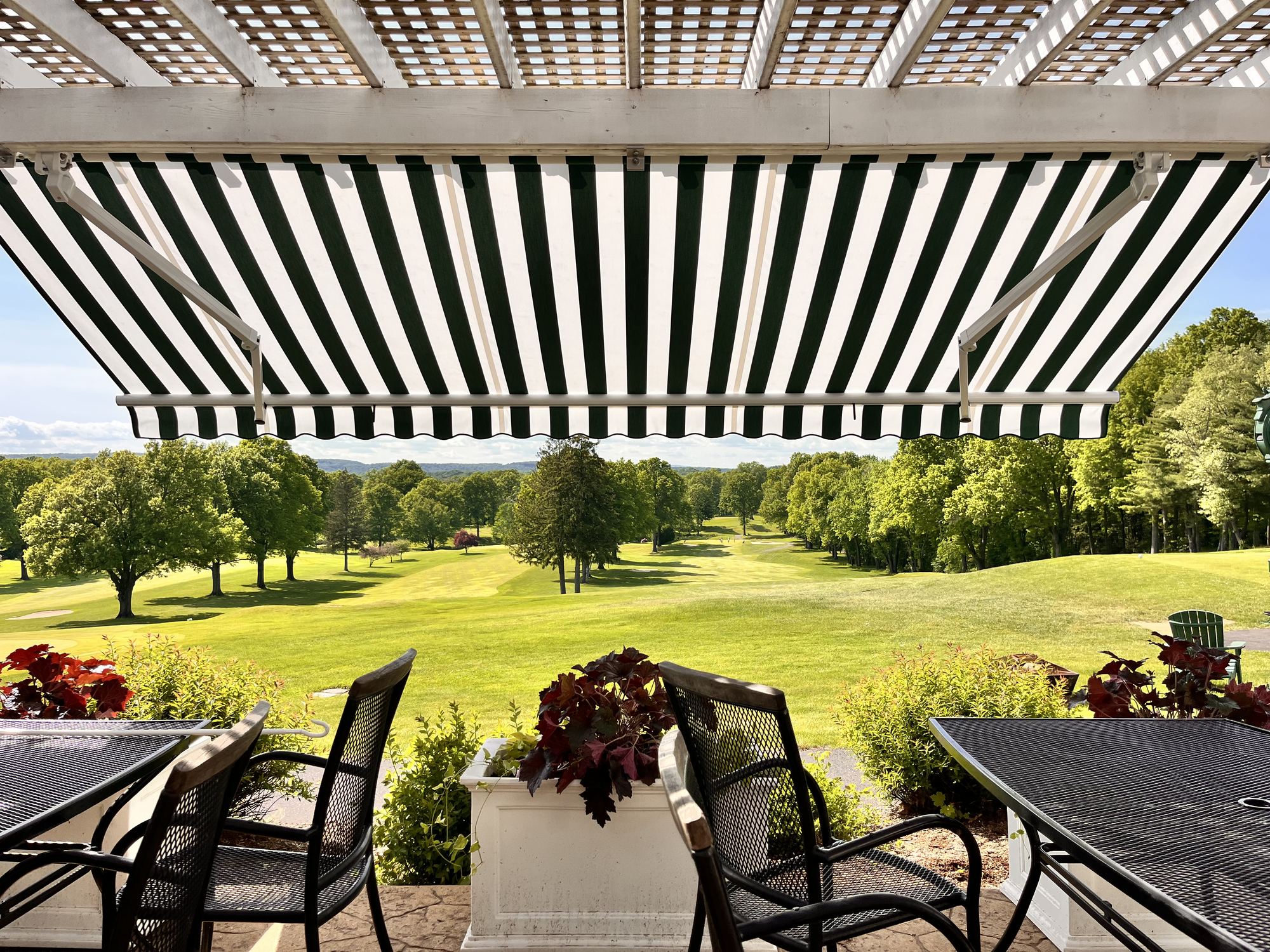 A bold green and white striped awning extended over a club terrace overlooking a fairway