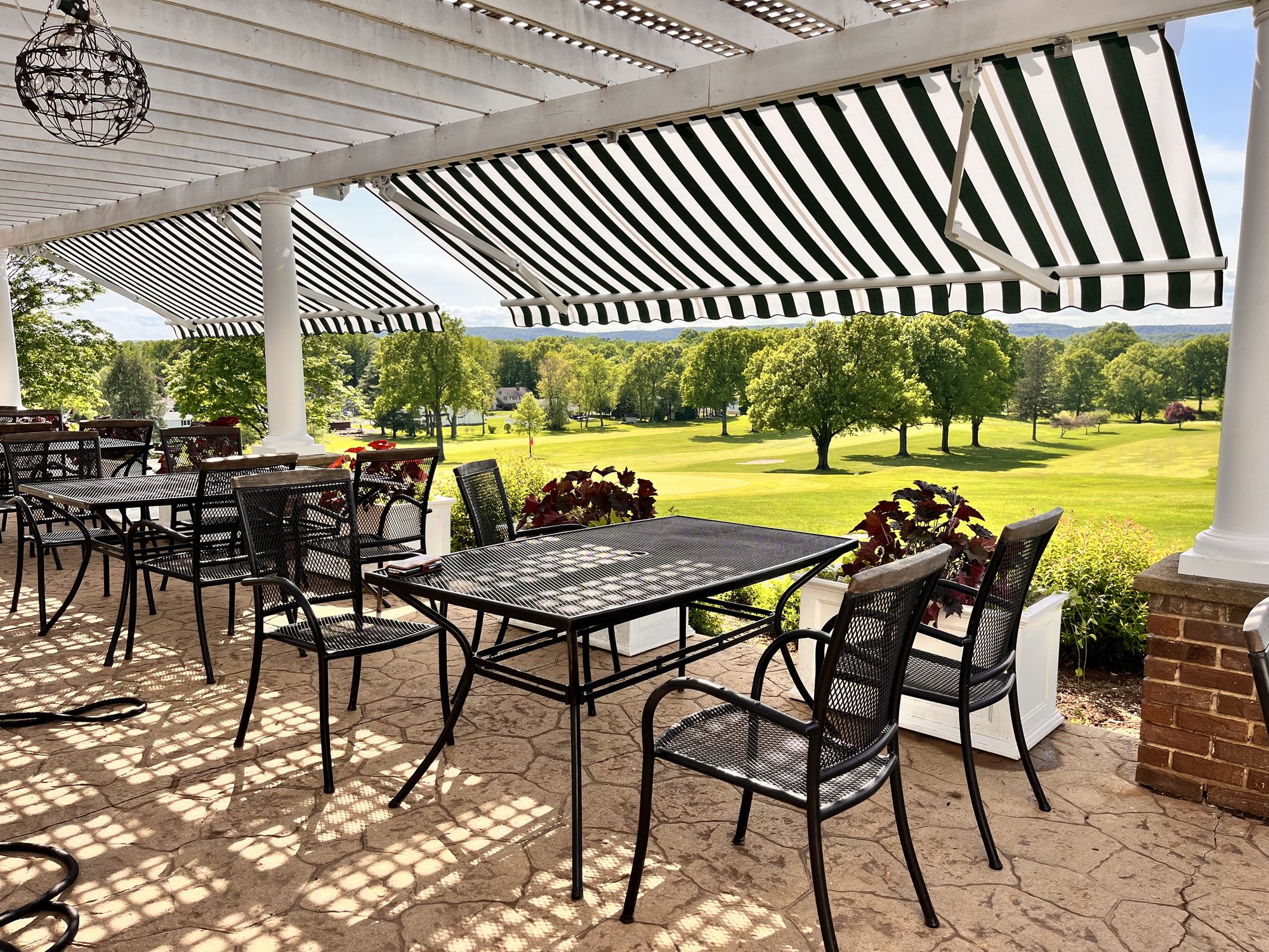 Underside of a green and white striped awning shading a paved patio, showing how the weave filters direct sun