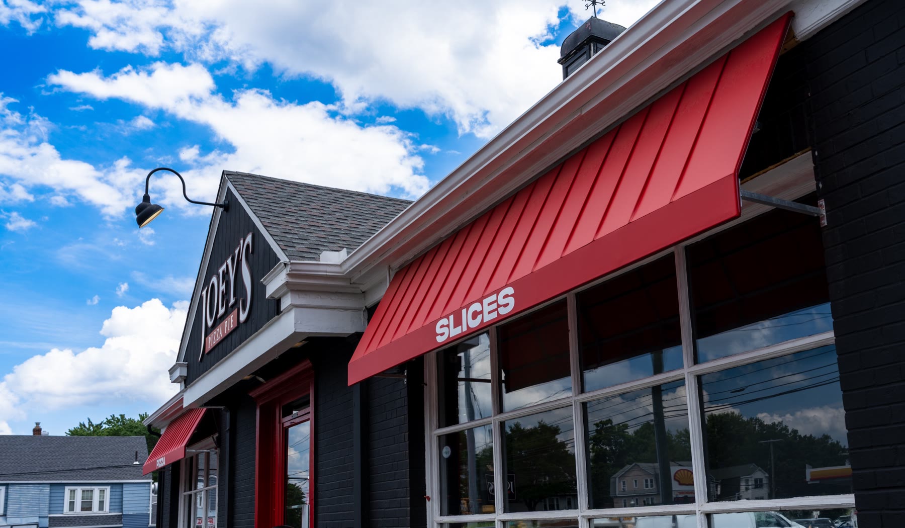 Close view of a deep red Metal Look awning showing the raised standing-seam ribs formed into the tensioned skin, with lettering applied to the fascia
