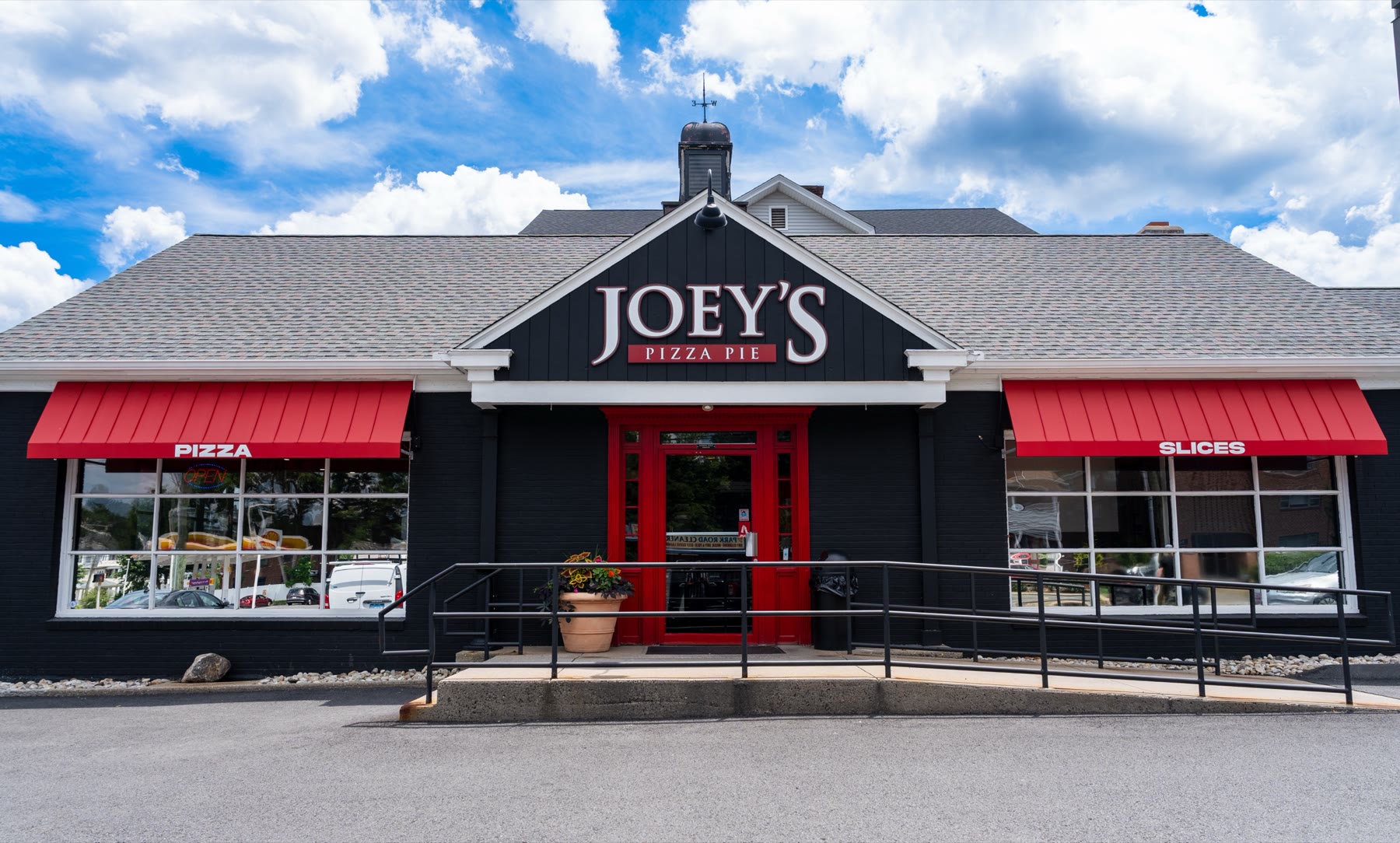 Front elevation of the Joey's Pizza Pie storefront with two deep red standing-seam Metal Look awnings over the windows and a matching entrance canopy