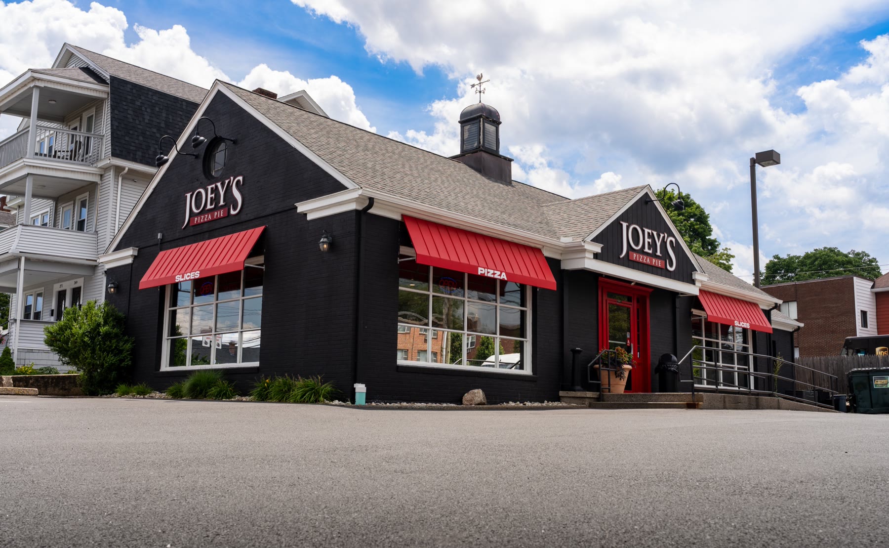 Wide view of the Joey's Pizza Pie building with deep red standing-seam Metal Look awnings across three elevations